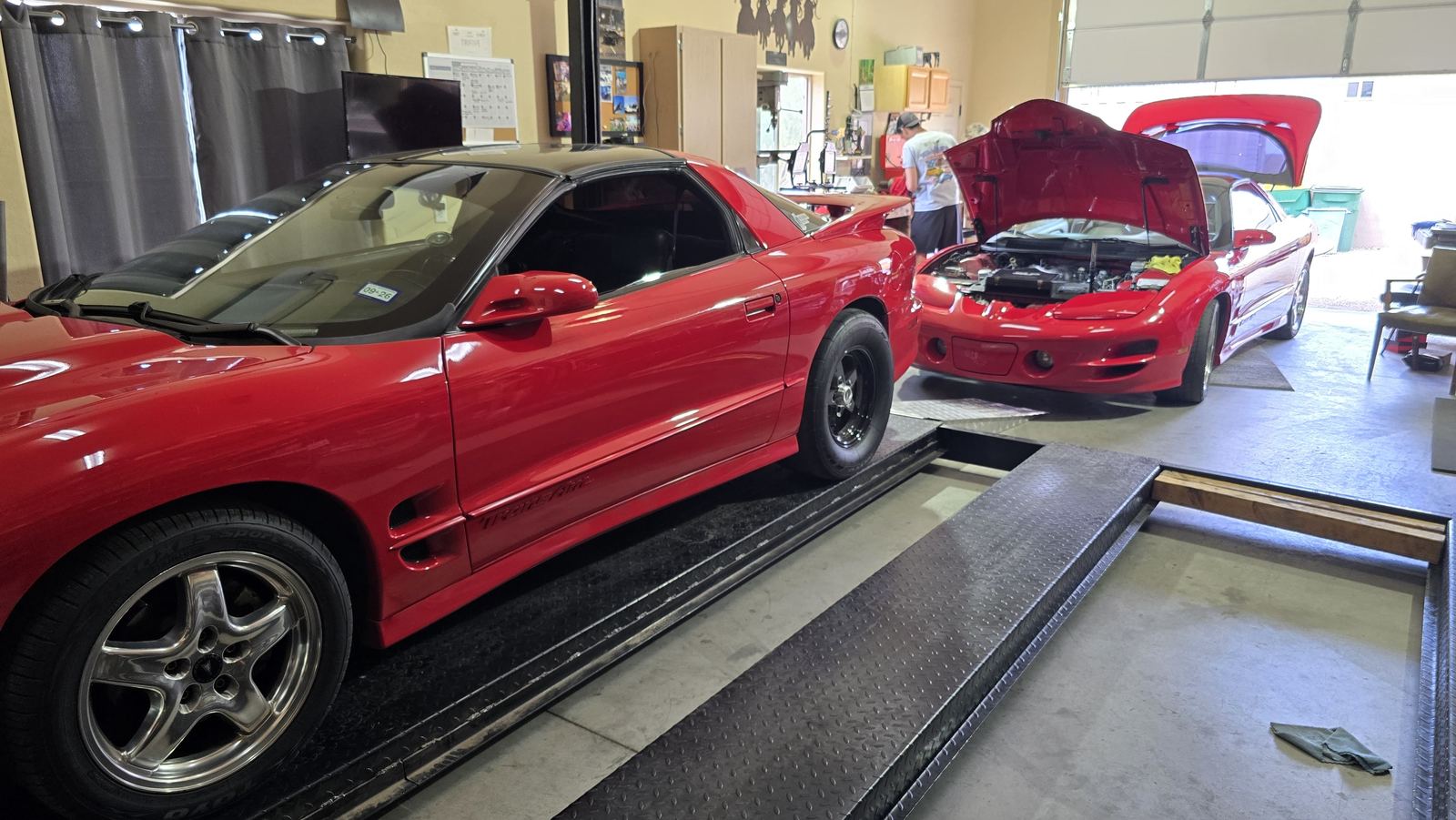 Two red Trans Ams in the shop, one with the hood up